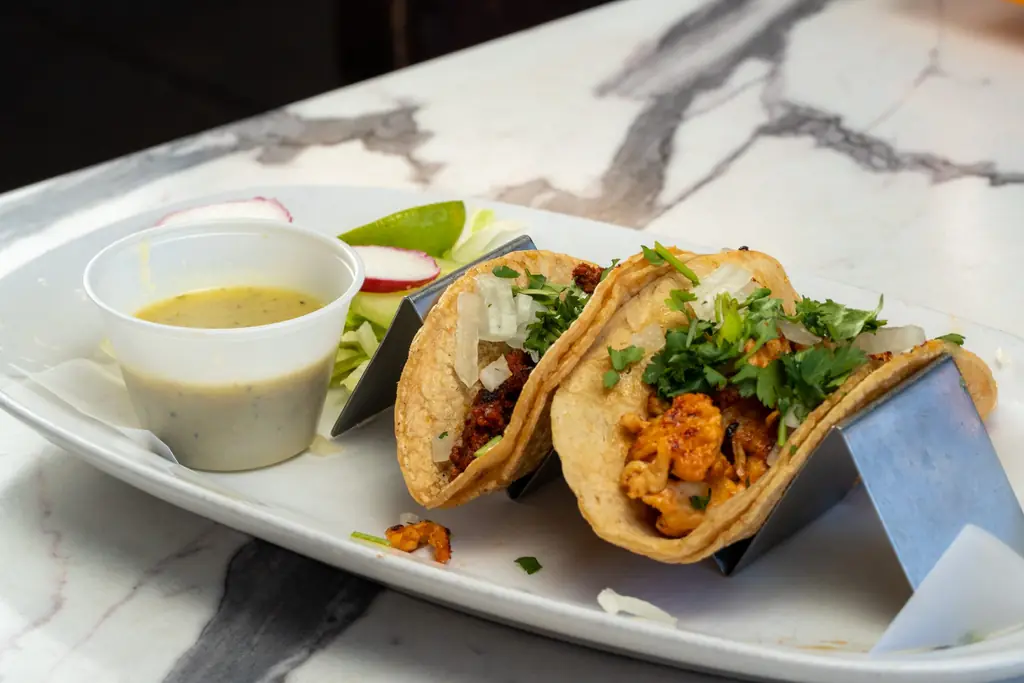 Tacos in a metal holder with salsa verde
