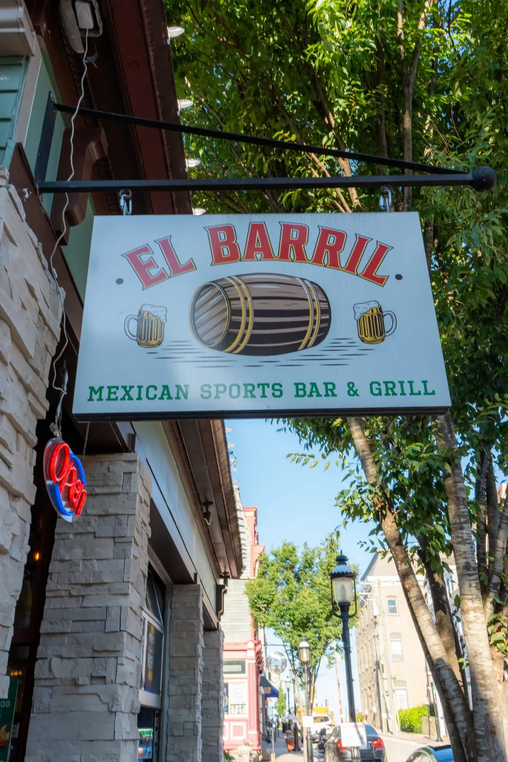 The hanging El Barril sign on Pavilion St with trees and the street behind